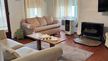 Ett vardagsrum med en beige soffa, ett soffbord, en öppen spis och en takfläkt.