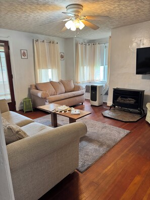 Ein Wohnzimmer mit beiger Couch, Couchtisch, Kamin und Deckenventilator.