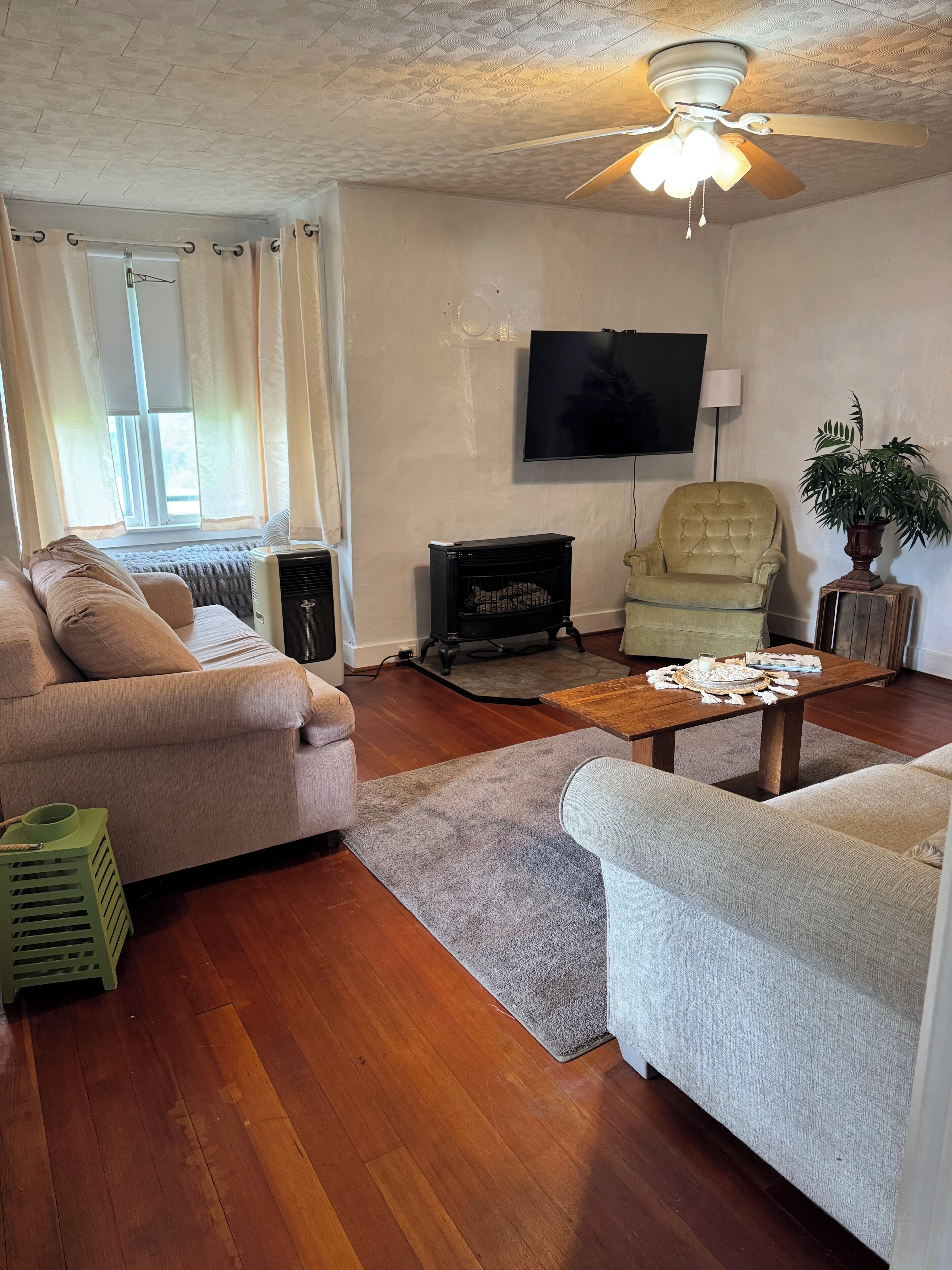 Ein Wohnzimmer mit Sofa, Sessel, Couchtisch aus Holz, Fernseher und Deckenventilator.