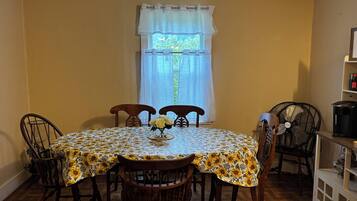 A dining area with a round table covered in a sunflower-patterned tablecloth, surrounded by wooden chairs.