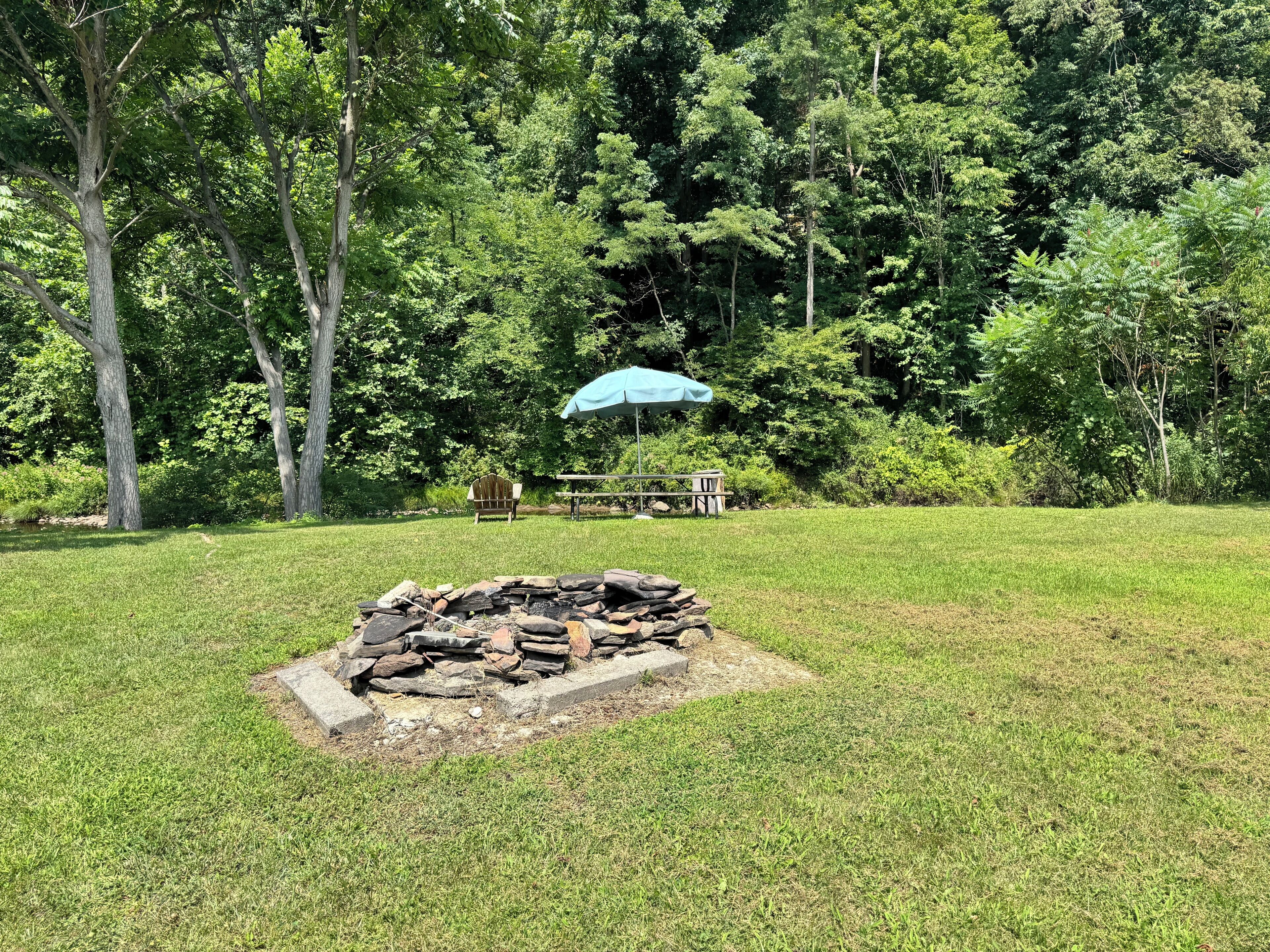 Un espacio al aire libre con césped, una chimenea de piedra, un banco de madera y un paraguas azul.