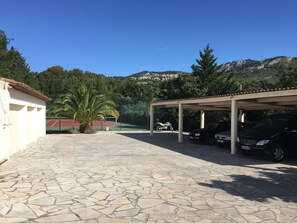 A covered parking area with a stone floor, a motorcycle, and a car parked under a shelter. - Detached studio apartment on a large property—in a residential neighborhood near the ocean (Ollioules)