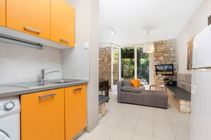 Eine moderne Küche mit orangefarbenen Schränken, einem eingebauten Backofen und einem Essbereich mit einem grauen Sofa und einem Fernseher.