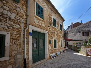 Un bâtiment en pierre avec une porte et des volets verts, une rue étroite et une enseigne indiquant un prix de 10 euros.