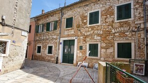 A stone building with multiple windows and a door, a paved courtyard, and a visible antenna. - Garden Apartment Orange I Porec Old Town (Porec)