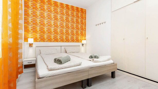 A bedroom with a bed, bedside tables, a wardrobe, and patterned wallpaper. - Garden Apartment Orange I Porec Old Town (Porec)