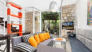 A modern living room with a sofa, a TV, and a stone wall. - Garden Apartment Orange I Porec Old Town (Porec)