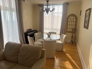 Un salon avec un canapé, une table en verre, des chaises, un piano et une fenêtre avec des rideaux.