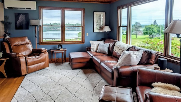 Un salon avec un canapé en cuir, un plafond en bois et de grandes fenêtres donnant sur un lac.