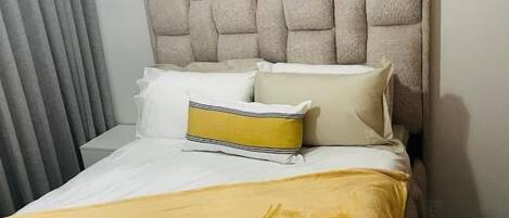 Habitación de hotel con cama, cabecero y ventana con cortinas.