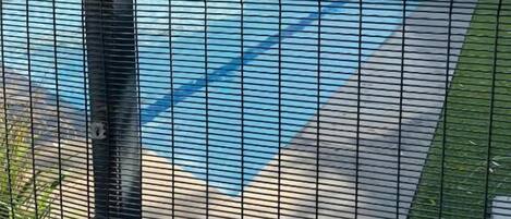 Una piscina con valla, un edificio con el número 48 y un paraguas rosa.