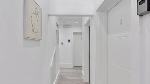 Un pasillo con suelo de madera, paredes blancas y una obra enmarcada a la izquierda.