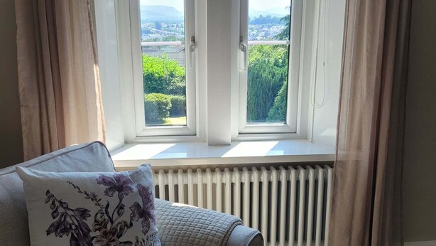 Une pièce avec une fenêtre, un radiateur et un canapé agrémenté d’un coussin à motifs floraux.