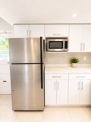 A kitchen with stainless steel appliances, white cabinets, and a potted plant on the countertop.