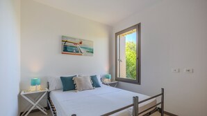 A bedroom with a bed, a window, a nightstand, and a wall-mounted painting. - Golden Stone Villa: Pool & Relax (Masainas)