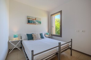 Ein Schlafzimmer mit einem Bett, einem Fenster, einem Nachttisch und einem Wandbild.