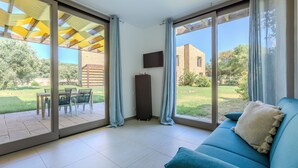A room with a blue sofa, a TV mounted on the wall, and a sliding glass door leading to an outdoor patio with a table and chairs. - Golden Stone Villa: Pool & Relax (Masainas)