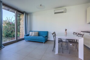 Ein modernes Wohnzimmer mit einem blauen Sofa, einem Esstisch mit Stühlen, einem großen Fenster mit Vorhängen und einer Wandklimaanlage.