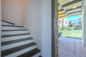 Un escalier menant à un espace extérieur abrité, d’où l’on peut admirer un bâtiment et une pelouse.