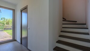 A staircase with a handrail, a door with a frosted glass panel, and a view of greenery outside. - Golden Stone Villa: Pool & Relax (Masainas)