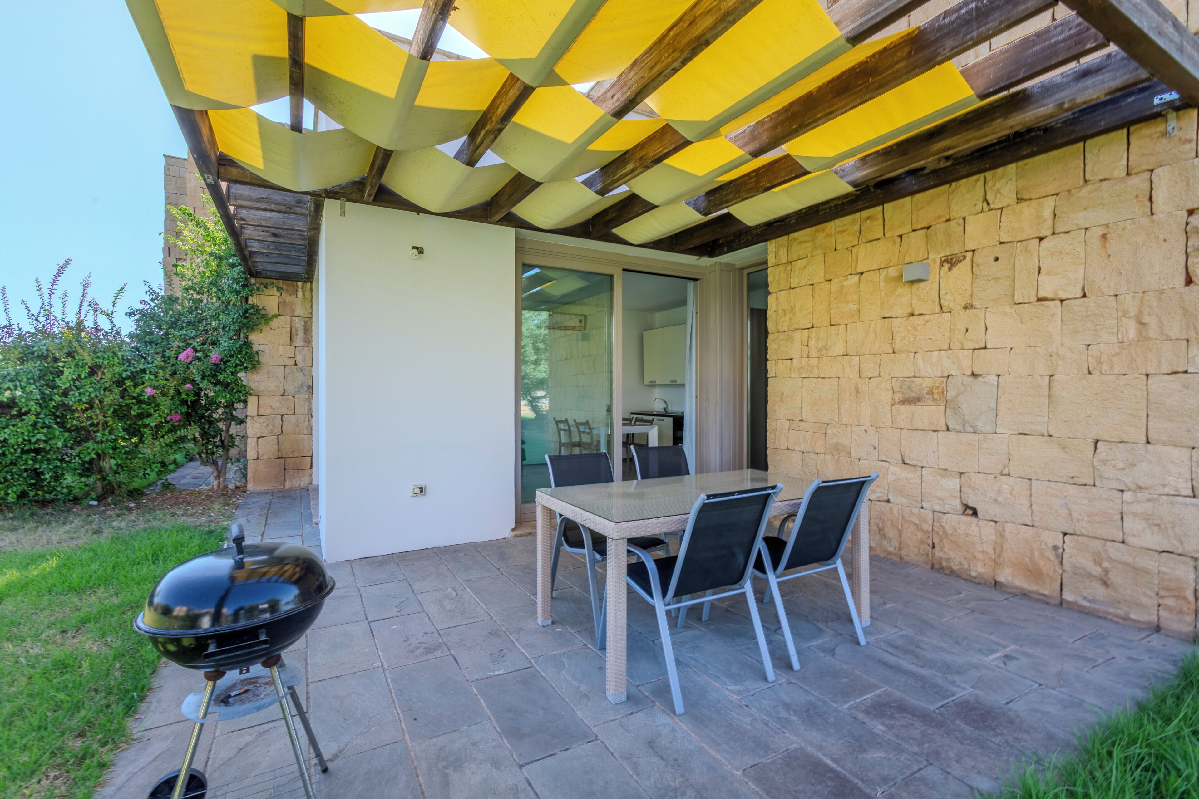 An outdoor patio with a table and chairs, a barbecue grill, and a stone wall.