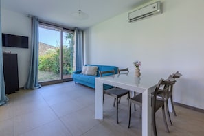 Un espace de vie moderne comprenant une table à manger, des chaises, un canapé, un téléviseur et une porte-fenêtre coulissante donnant sur un jardin.