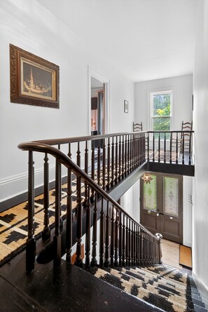 A staircase with a black and beige patterned carpet, a wooden railing, and a door with decorative glass panels. - FLX Victorian, Historical Charm + Modern Comfort, Perfect Location to Everything (Ovid)