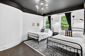 Ein Schlafzimmer mit zwei Betten, einem gemusterten Teppich, einer Kronleuchter und einem Fenster mit Vorhängen.