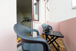 A small outdoor seating area with a table and two chairs, a window, and a kitchen visible in the background.