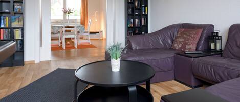 A living room with a sofa, a coffee table, a bookshelf, and a dining area with a table and chairs.