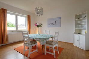 A dining area with a table set for four, a vase with flowers, a painting on the wall, and a cabinet with glassware.