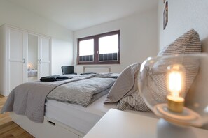 Ein Schlafzimmer mit einem Bett, einem Fenster, einem Sessel und einem Nachttisch mit einer Lampe.