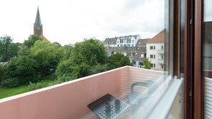 Un balcone con tavolo e sedie, affaccia su una zona residenziale con case e il campanile di una chiesa.