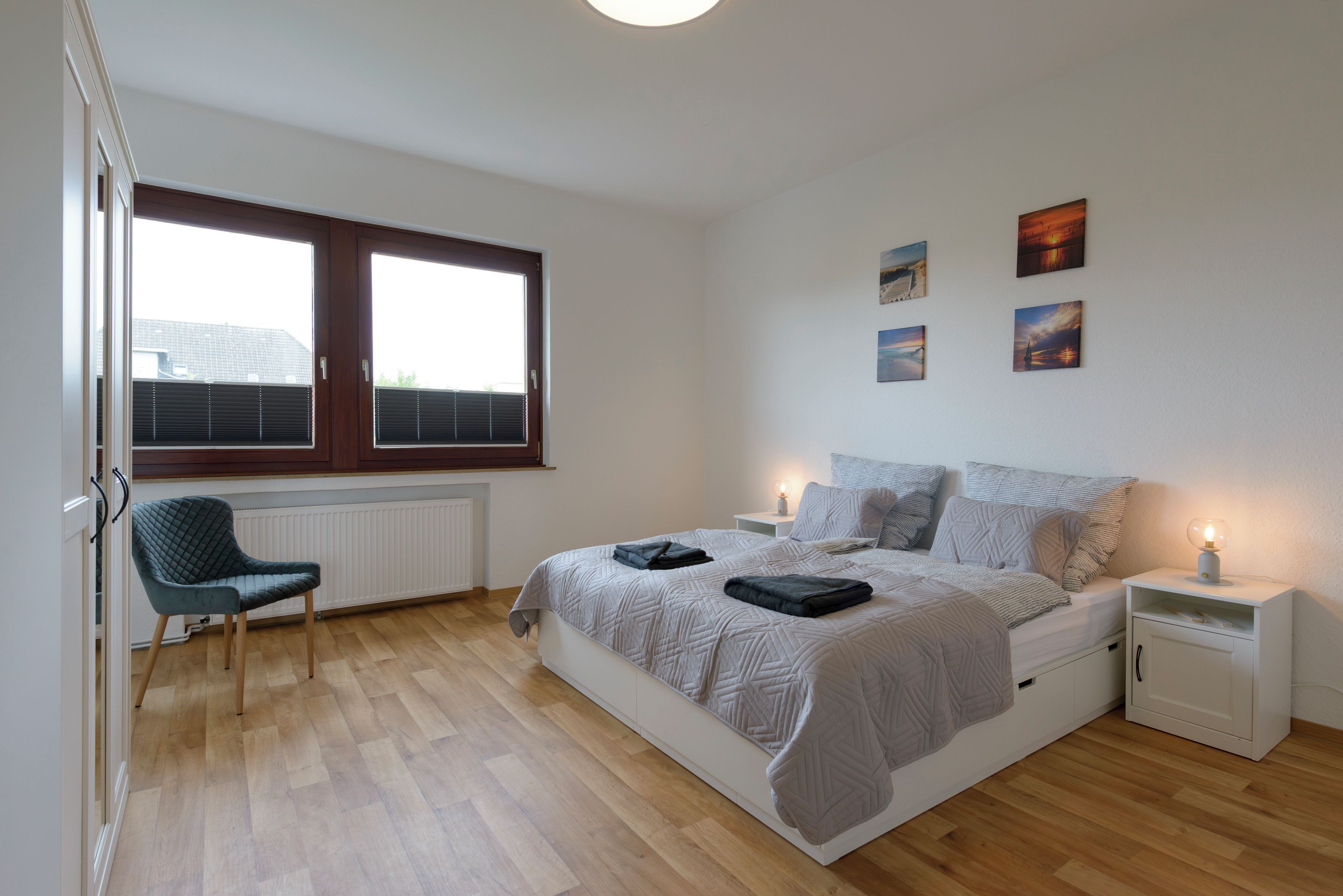 A bedroom with a bed, bedside tables, a chair, and artwork on the wall.