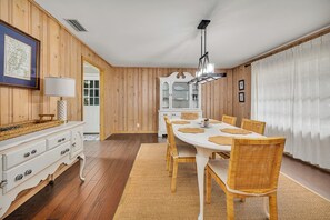 Ein Essbereich mit einem weißen Tisch, Korbstühlen und einem weißen Schrank mit Schubladen.