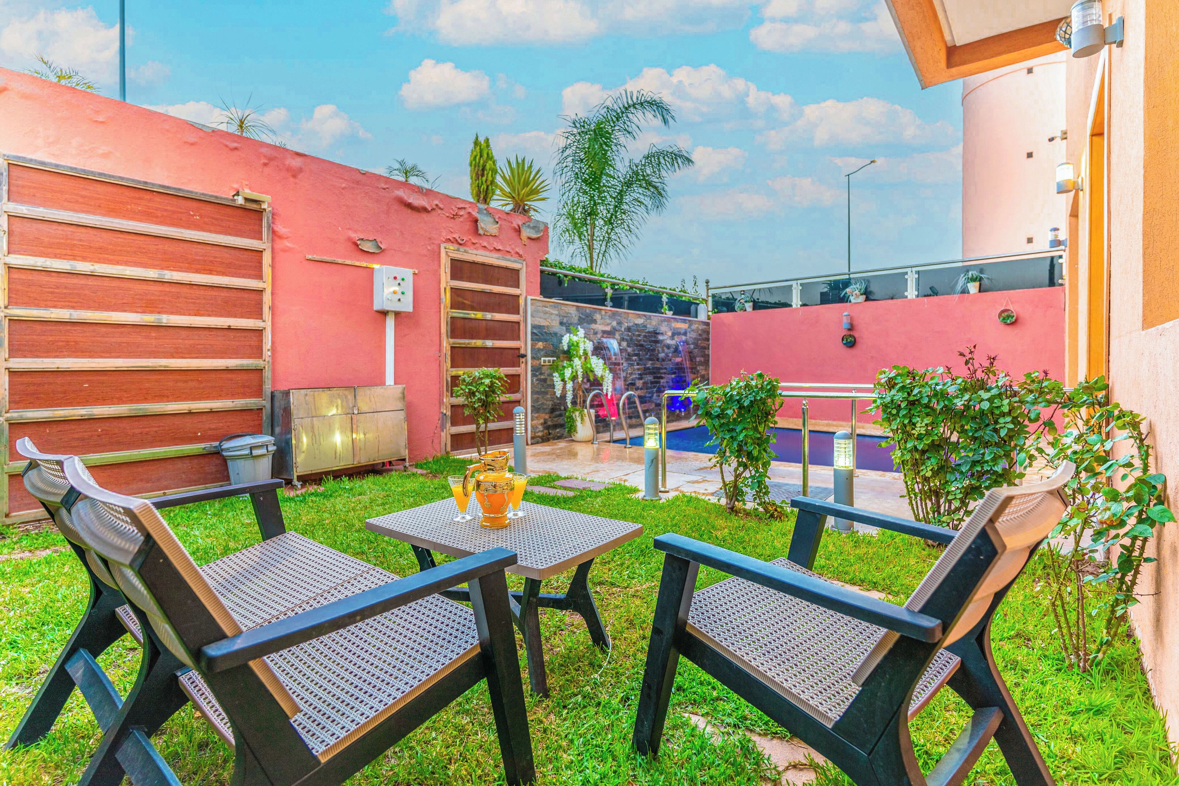 An outdoor seating area with two tables and four chairs, a small pool, and a stone wall with a metal gate.
