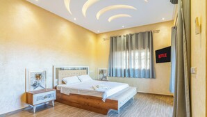 A modern bedroom with a wooden bed, bedside tables, a wall-mounted TV, and a large window with curtains. - Fabulous 3-bedroom house with AC in vibrant Marrakech (Marrakech)