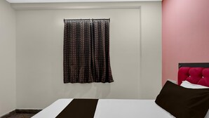 Habitación de hotel con cama, ventana con cortinas estampadas y una pared de acento roja.