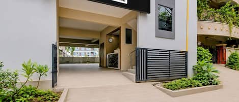 A hotel entrance with a sign reading 'HOTEL OYO-Serviced,' a modern building facade, and a gated entrance.