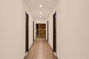 A hallway with wooden flooring, white walls, and doors on both sides leading to a room with a wardrobe and shelves. - Hotel O Visakhapatnam Railway Junction (Visakhapatnam)