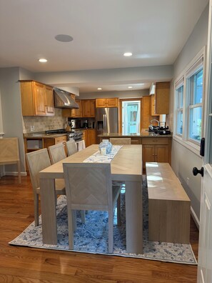 A modern kitchen with wooden cabinets, a stainless steel refrigerator, and a dining area with a large table and chairs. - Spacious 5-bedroom house in Falmouth within walking distance to Beach and Town (Falmouth)