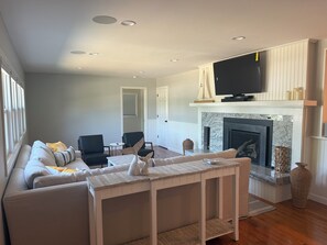 A living room with a sofa, chairs, a TV, a fireplace, and a dining table. - Spacious 5-bedroom house in Falmouth within walking distance to Beach and Town (Falmouth)