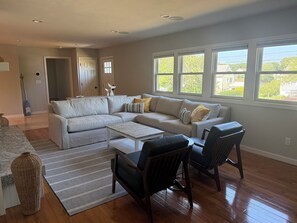 A living room with a sectional sofa, a coffee table, two armchairs, a rug, and a large window with a view of greenery. - Spacious 5-bedroom house in Falmouth within walking distance to Beach and Town (Falmouth)