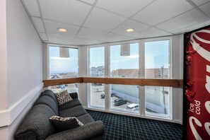 A room with a large window, a gray sofa, and a view of the cityscape.