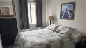 A bedroom with a bed, a dresser, a window with curtains, a lamp, and a picture on the wall.