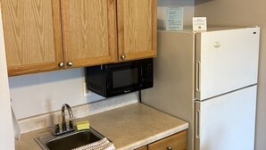 A kitchen with wooden cabinets, a black microwave, a white refrigerator, and a stainless steel sink.