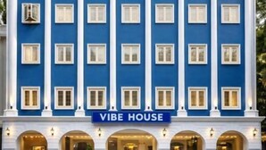 Un edificio de varios pisos con fachada azul, un letrero que dice 'VIBE HOUSE' y varios comercios en la planta baja.