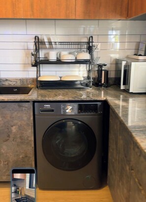 A kitchen with a built-in washer and dryer, a dish rack, and a countertop with a coffee maker. - Cozy Lake View Haven (Kampala)