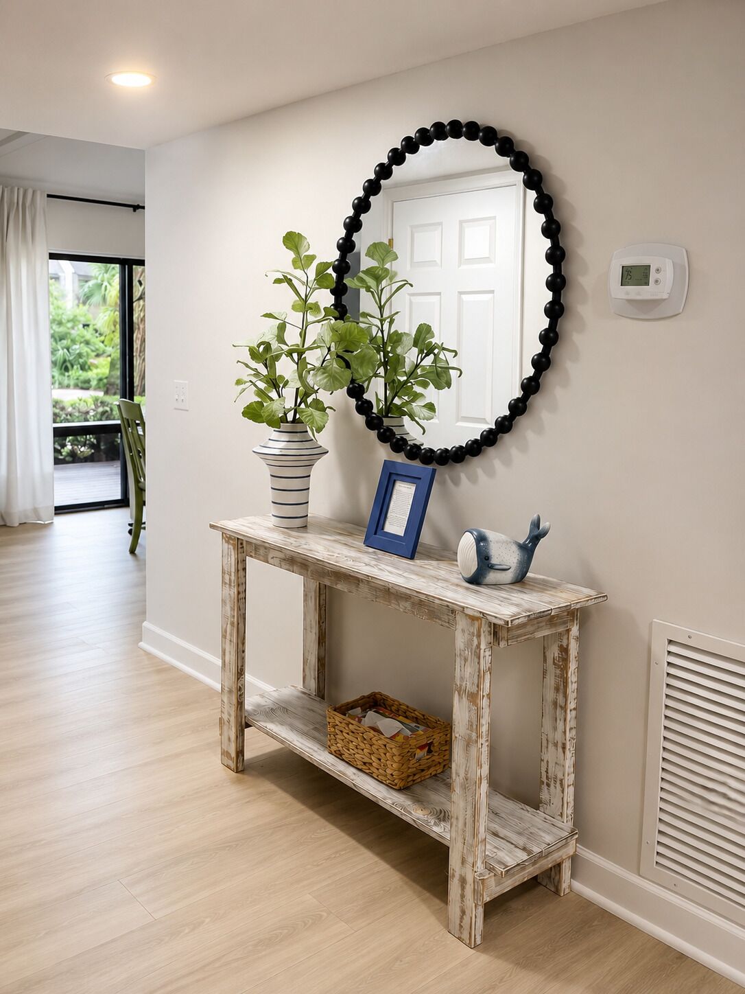 Un couloir avec une console en bois rustique, un miroir, une plante en pot, un tableau encadré et un thermostat fixé au mur.