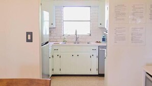 Une cuisine avec des meubles blancs, une fenêtre et un luminaire suspendu.